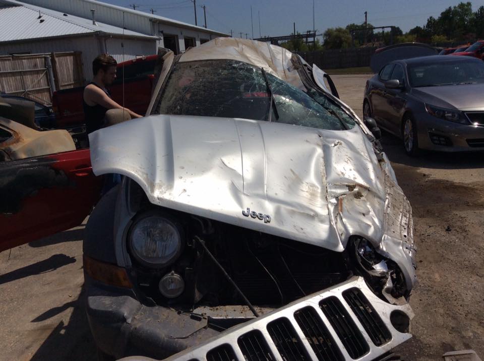 Photo of a young man standing behind a very wrecked Jeep 