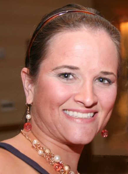 Amanda has her dark hair pulled back. She is wearing a necklace and dangly earrings with a big smile aimed at the camera.
