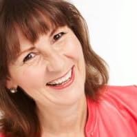Mary has long brown hair and is smiling at the camera in her coral-colored blouse.