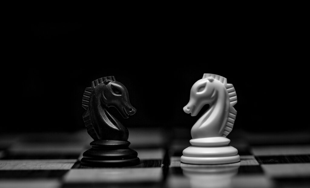 two figurines: A white knight and a black knight, face each other on a chessboard
