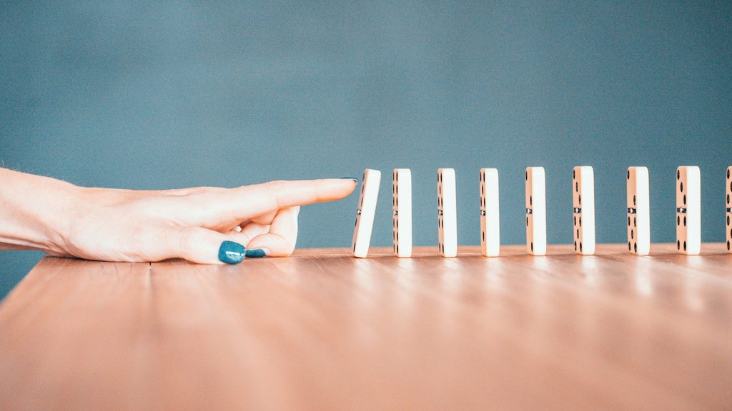 A woman's hand moving toward a line of dominoes, starting the first domino to tip into the line.